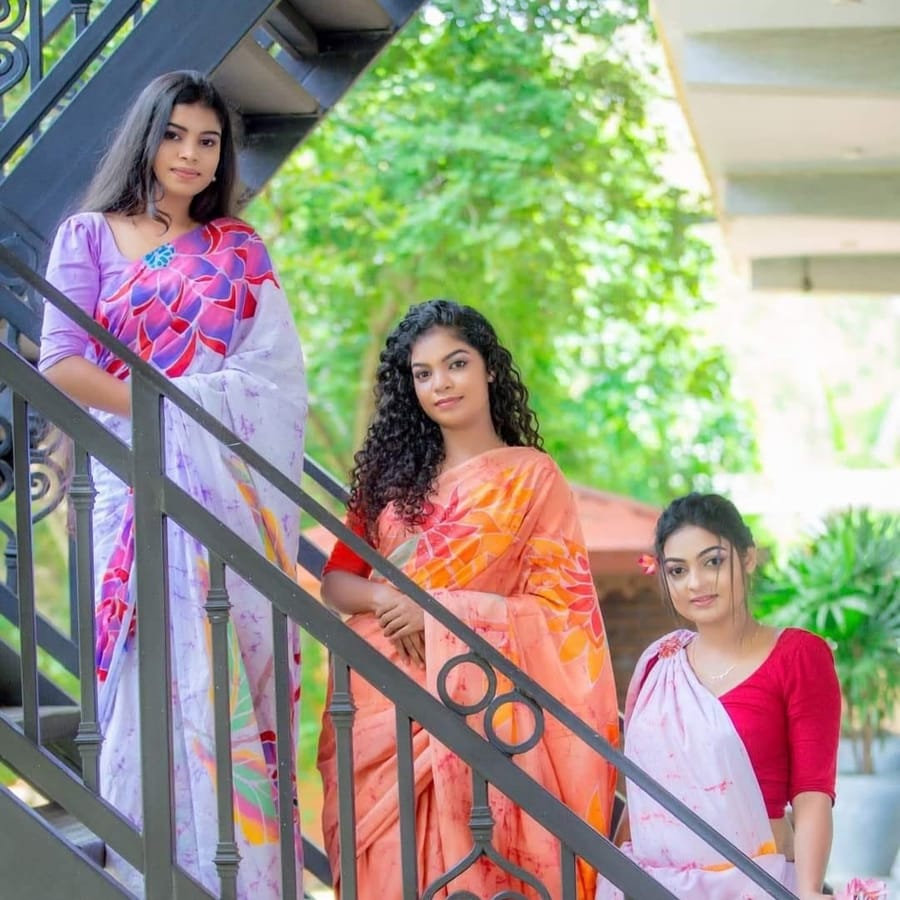 Three women on a staircase wearing hand-drawn Kithwari batik sarees